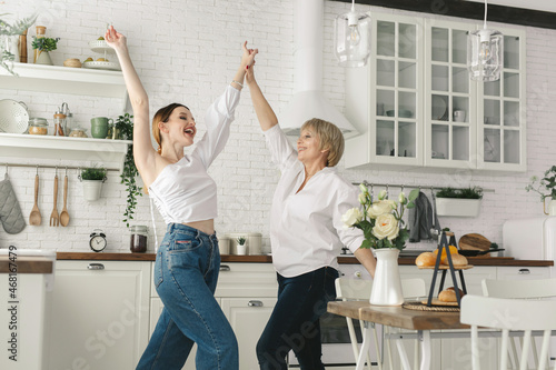 Mother and her adult daughter are having fun and dancing in the kitchen