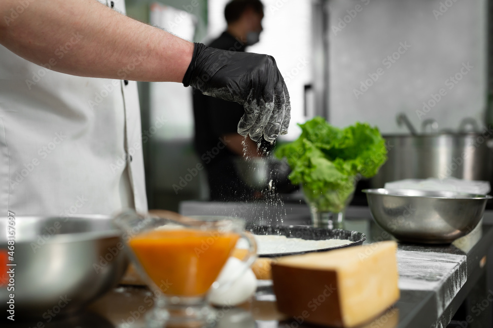 Preparation of the dough for pizza. Close-up of the cook's hand sprinkling the dough with flour Preparation of the dough for pizza. Close-up of the cook's hand sprinkling the dough with flour