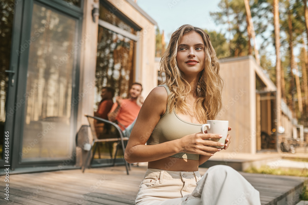 Fototapeta premium Woman with cup sitting on porch of house