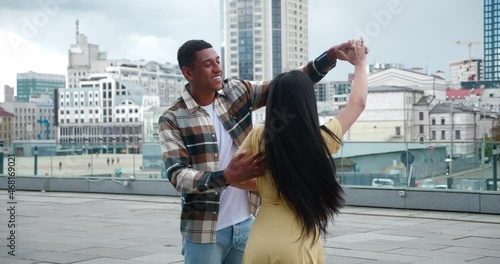Beautiful multi-ethnic couple of two young people dancing and enjoying romantic date on the rooftop of an urban building. Handsome African guy turning his girlfriend around herself while dancing