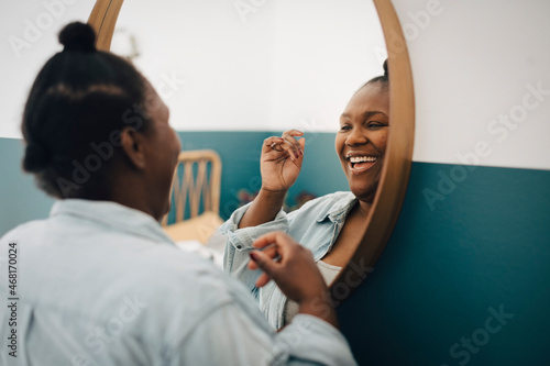 Happy mid adult woman looking in mirror at home