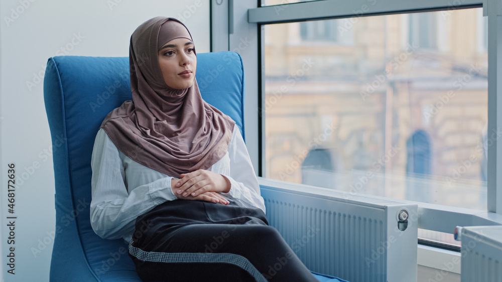Arabic female Intern student in hijab waiting for exam or interview results in armchair. Job candidate sits at recruit agent office expecting meeting with employer for hiring. HR, career concept Arabic female Intern student in hijab waiting for exam or interview results in armchair. Job candidate sits at recruit agent office expecting meeting with employer for hiring. HR, career concept