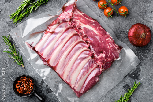 Raw frenched rack of lamb organic meat in sealed plastic wrapping, on gray stone table background, top view flat lay
