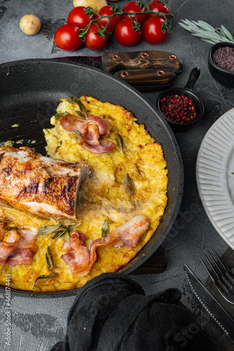 Roasted pork loin with mash potatoe gratin, sage and prosciutto, on frying cast iron pan and plate, on gray stone background