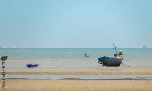fisherman's fishing boat on sand at a fishing village beach There is an island and sea background with the daytime sky.  stranded fishing boat After the sea has receded © Kullaya