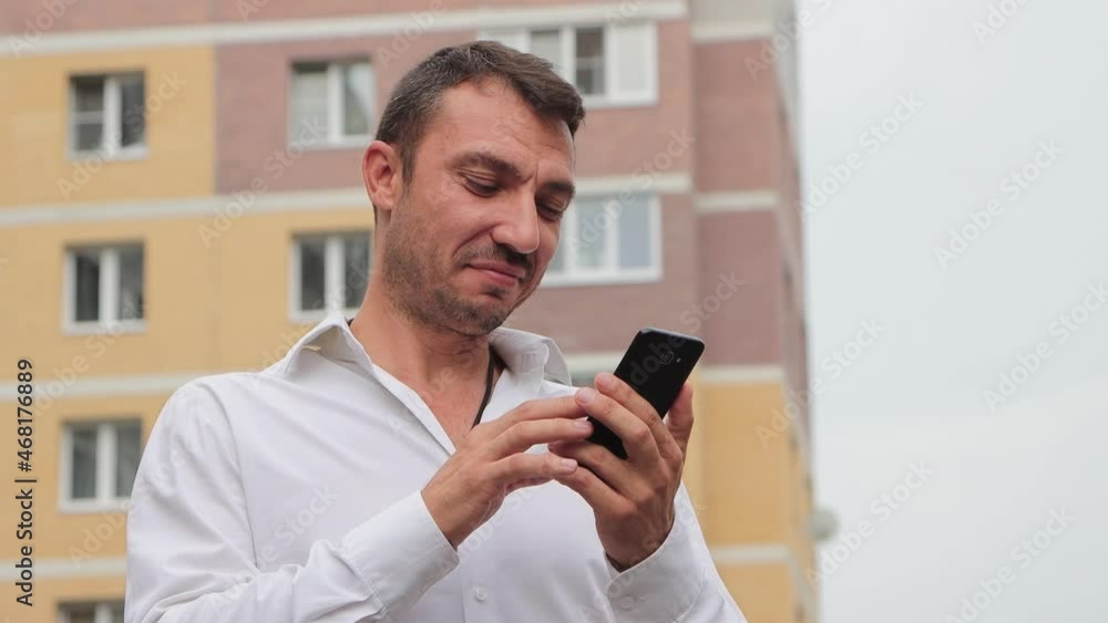 Close-up of a happy businessman laughing and dialing the number. Young man in the city center against the background of high-rise buildings. The concept of business and professional activities. 4K UHD Close-up of a happy businessman laughing and dialing the number. Young man in the city center against the background of high-rise buildings. The concept of business and professional activities. 4K UHD