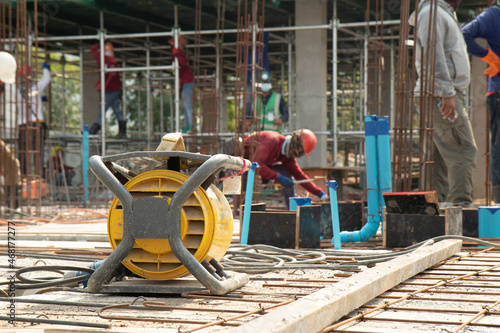 Yellow concrete vibrater on rebar for floor pouring frame in construction area, background with columnar and building condition during construction.