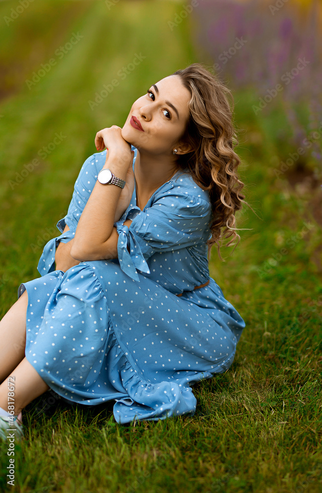 Obraz premium portrait of a young caucasian curly-haired woman in a long blue dress, european lady in a blooming field