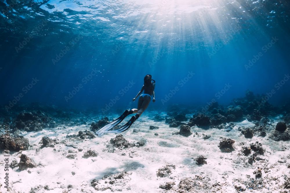 Freediver woman in bikini with fins glides underwater in tropical ocean