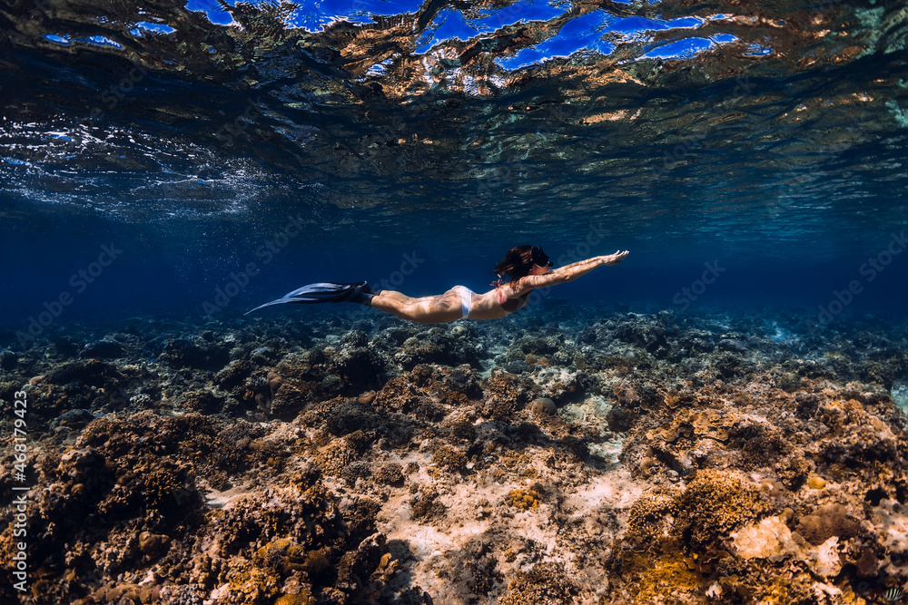 Woman freediver with fins glides over coral reef underwater in ocean. Freediving in tropical sea