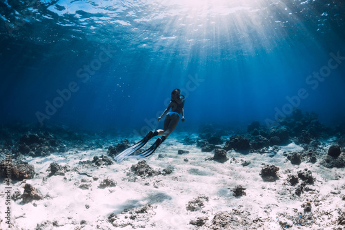 Freediver woman in bikini with fins glides underwater in tropical ocean