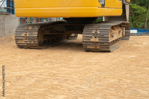 The backhoe's steel yellow colour on iron, parked on the ground in a construction site.