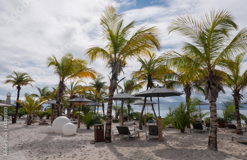A deserted beach on Bonaire. In the background the dark clouds of the heavy rain shower on the beach are still visible. The raindrops are on the umbrellas, and beach chairs are still wet. © Alie