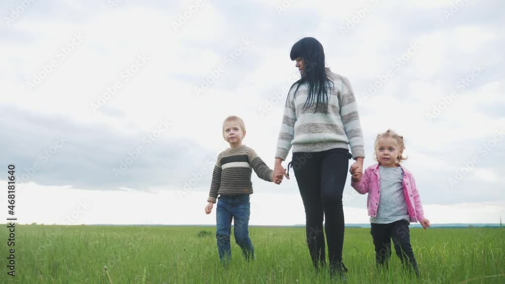 happy family lifestyle. mom and little children walk in the park teamwork outdoors holding hands. woman and little boy and girl walking on a green field at sunset happy family lifestyle. mom and little children walk in the park teamwork outdoors holding hands. woman and little boy and girl walking on a green field at sunset