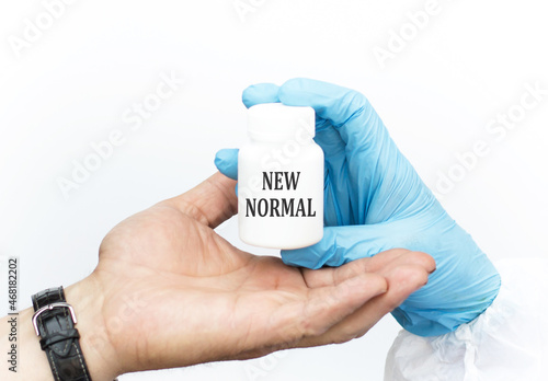 Medicine concept. NEW NORMAL inscription on the jar, which is held in the hands of the doctor and passes it to the patient, close-up of the hand on a white background