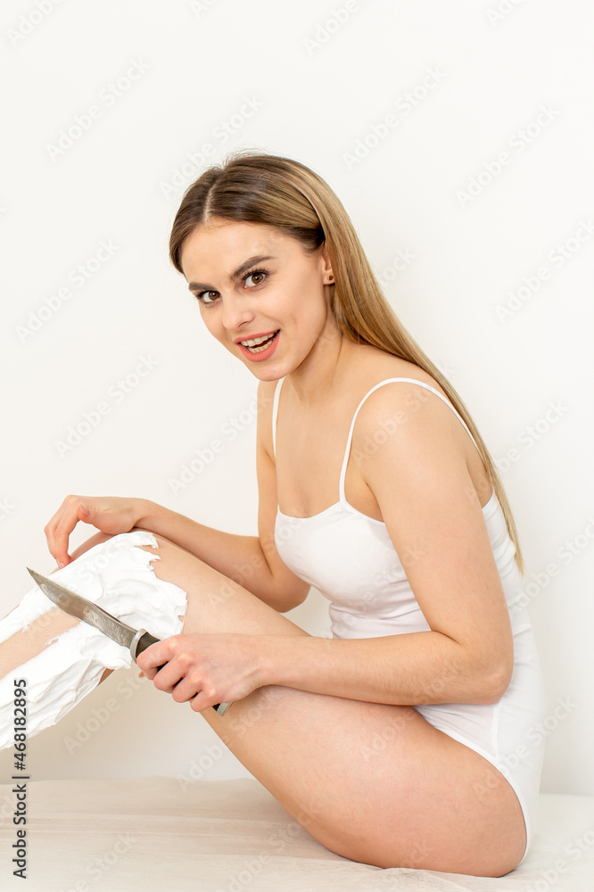 Beautiful caucasian woman shaving her legs with a knife with shaving foam on white background. Depilation and epilation concept Beautiful caucasian woman shaving her legs with a knife with shaving foam on white background. Depilation and epilation concept