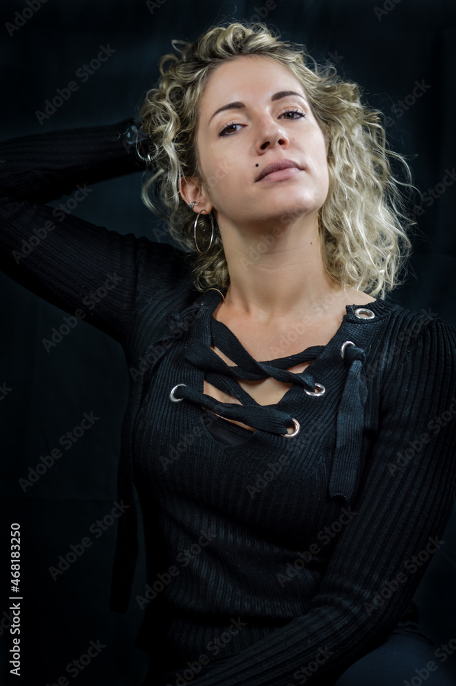Portrait of a beautiful young woman with blond curly hair who holds her hair behind her neck with her hand and looks haughty in front of her Portrait of a beautiful young woman with blond curly hair who holds her hair behind her neck with her hand and looks haughty in front of her