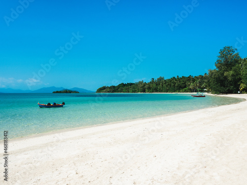 Scenic view of peaceful white sand beach tropical island with crystal clear turquoise water and fishing boat against blue sky. Koh Mak Island, Trat, Thailand.