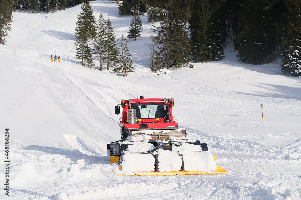 red tractor of municipal service in mountains of Swiss Alps with wide snow shovel clears the road from heavy snow, Winter Activity Concept, travel by car, problems of utilities in winter