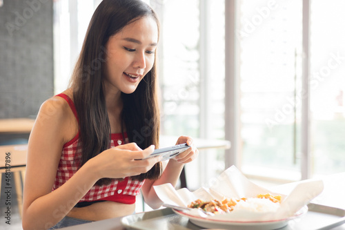 Young attractive asian teen female influencer, foodie blogger take photo of food  .keep social distance for protect infection from coronavirus covid-19, restaurant and social distancing concept. photo