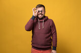 Cheerful Caucasian bearded man holds toy sunglasses like pince-nez to his eyes, with a bizarre grimace and grin. Yellow background.