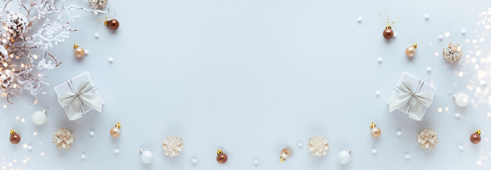 Christmas or New Year concept with gift box, festive baubles and snowy branch with pine cones on pastel background. Flat lay, copy space.
