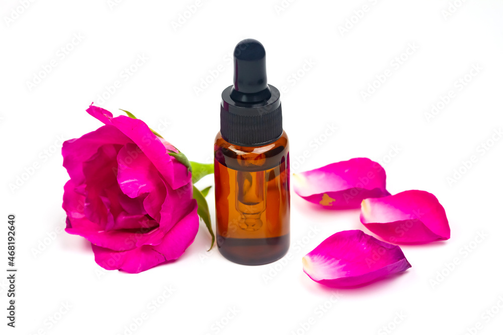 Rose oil in glass bottle and rose flower isolated on white background. Essential oil product concept. Rose oil in glass bottle and rose flower isolated on white background. Essential oil product concept.