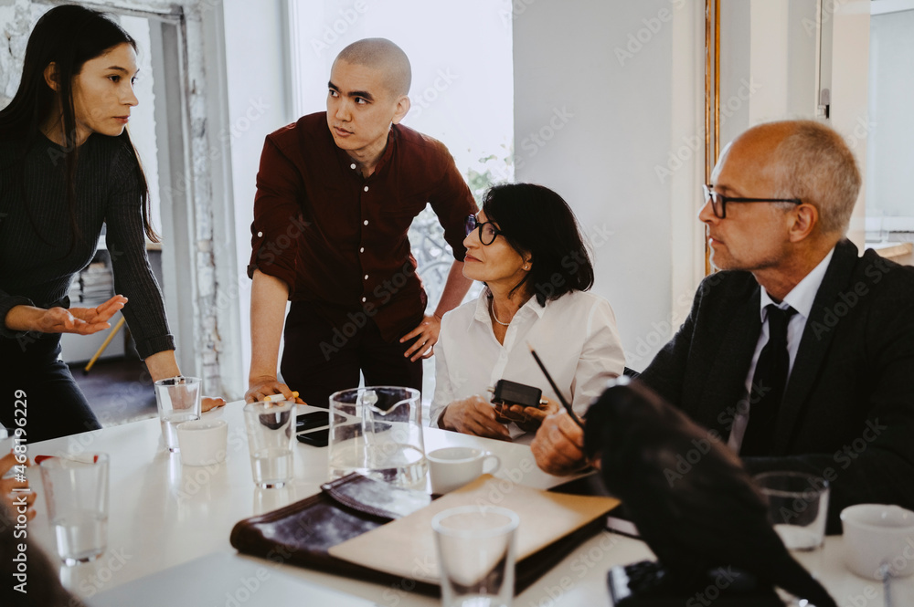 Male and female programmers discussing with advisors at table in office Male and female programmers discussing with advisors at table in office