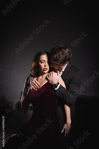 passionate woman in elegant dress near man in suit seducing her in darkness