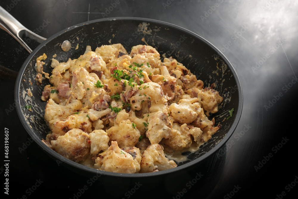Frying pan with cauliflower florets, ham and a sauce from cream, cheese and egg, parsley garnish, cooking with vegetables for a ketogenic or low carb diet meal, selected focus Frying pan with cauliflower florets, ham and a sauce from cream, cheese and egg, parsley garnish, cooking with vegetables for a ketogenic or low carb diet meal, selected focus
