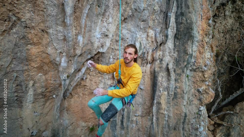 slow motion of joyful handsome man rock climber in yellow sweatshirt with long hair hanging on rope and give high five after successful ascent of route on cliff. slow motion of joyful handsome man rock climber in yellow sweatshirt with long hair hanging on rope and give high five after successful ascent of route on cliff.