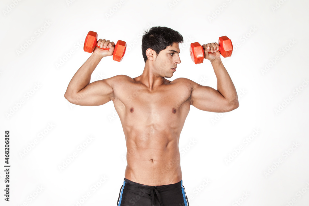 Portrait of shirtless sexy sportsman looking away, standing with raised arms, holding dumbbells, having workout for biceps and triceps. Indoor studio shot isolated on white background.
