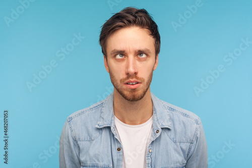 Portrait of comic positive handsome man wearing denim shirt, looking cross-eyed, having fun with silly face expression, playing fool. Indoor studio shot isolated on blue background. © khosrork