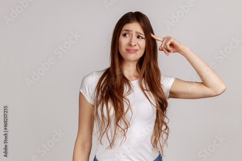 Portrait of displeased woman showing stupid gesture, accusing dumb reckless suggestion, crazy plan for idiots, wearing white T-shirt. Indoor studio shot isolated on gray background. photo