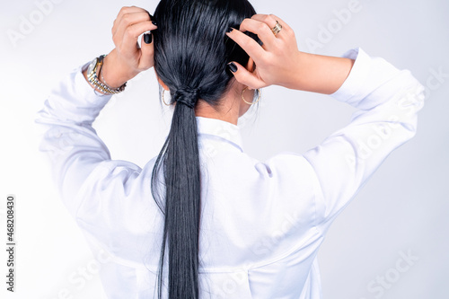 Back view photo of a woman in a white t-shirt with gold watch on her hand and the ring straightens long black tail.