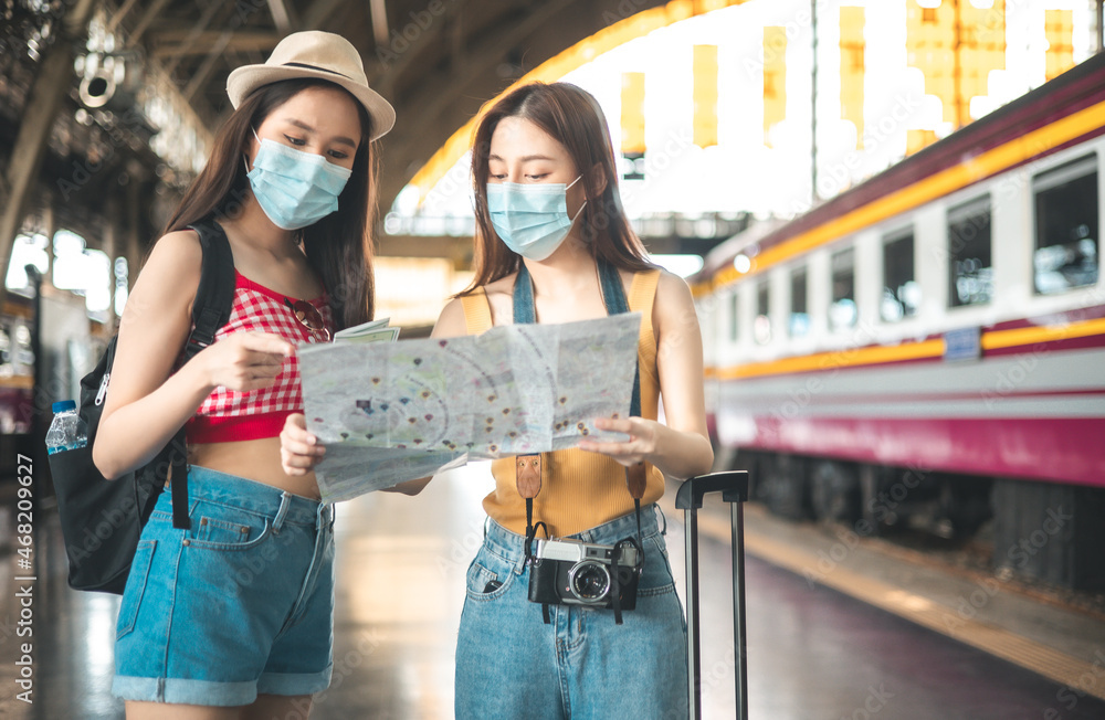 Fototapeta premium Asian backpack traveler people with camera standing at train station platform and waiting train arrivel, summer holiday travelling looking down at the map, travel concept.
