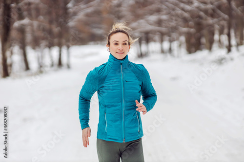 Fit sportswoman running in nature on a snowy path. Cold weather, snow, healthy life, fitness