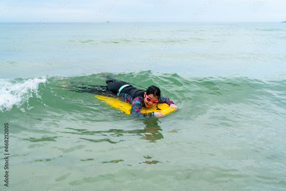 cute asian girl wearing a black swimsuit running on the waveboard surf in the sea on a bright day