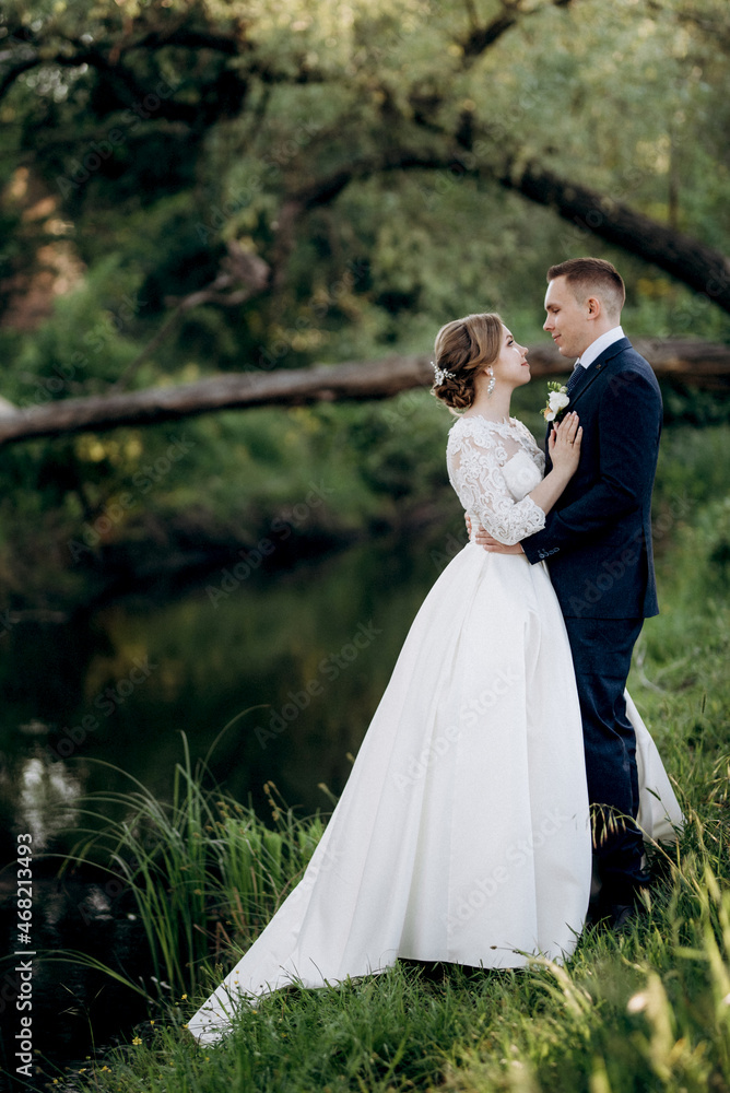 the groom and the bride are walking in the forest near a narrow river