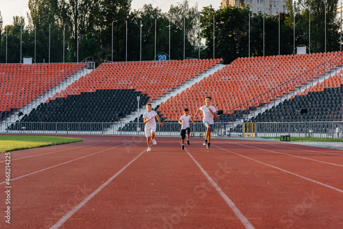 A large group of boys ' children are taught by a coach at the start before running at the stadium during sunset. A healthy lifestyle.