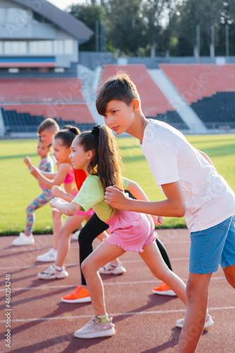 A large group of children, boys and girls, run and play sports at the stadium during sunset. A healthy lifestyle.