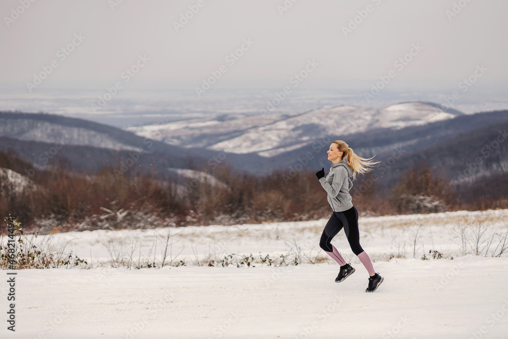 Sportswoman jogging in nature at snowy winter day. Healthy lifestyle, winter fitness