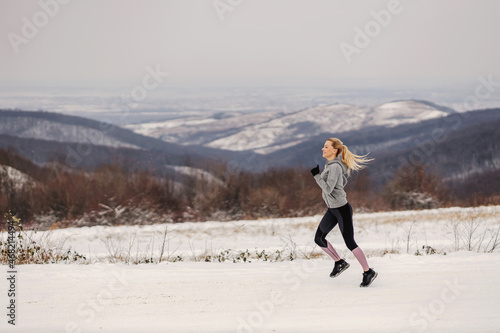 Sportswoman jogging in nature at snowy winter day. Healthy lifestyle, winter fitness
