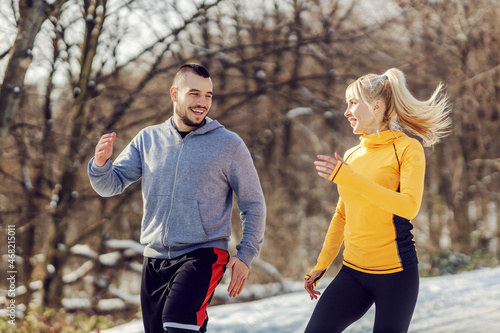 Happy sporty couple running in nature together at snowy winter day. Healthy lifestyle, winter fitness, relationship