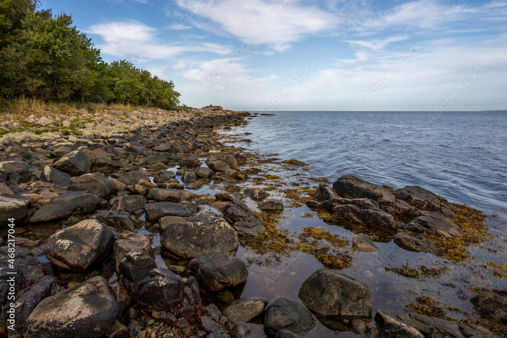 A rocky shoreline with blue water and a blu sky in the background. Picture from Skalderviken, southern Sweden