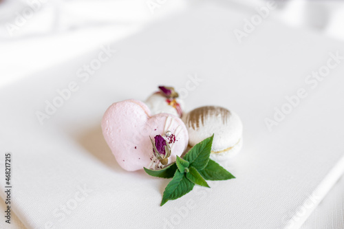 Beautiful tender delicious pastries with a green leaf on a light background. White and pink macaroons on a white canvas. Valentines Day background