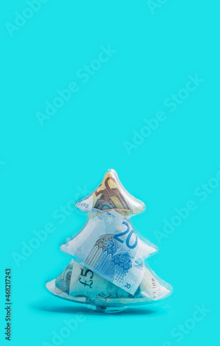 New year inspired concept. Funky christmas tree full of paper banknotes, bright blue background.