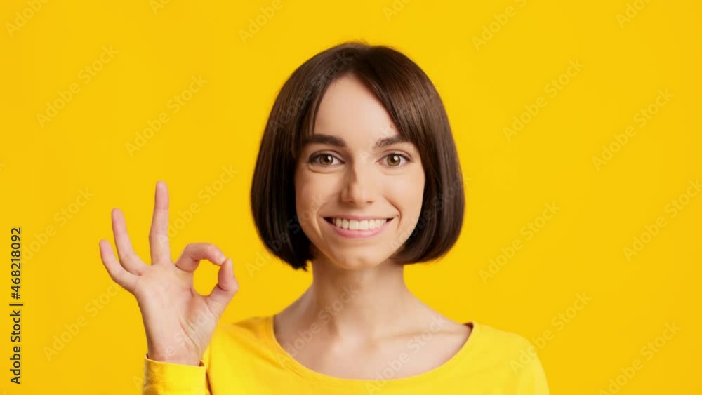 Cheerful Young Lady Gesturing And Saying OK Over Yellow Background Cheerful Young Lady Gesturing And Saying OK Over Yellow Background