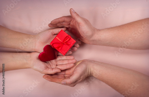 Male and female holds Heart and gift box with red ribbon on brown light background