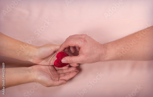 Valentine day consept A in man hand give to female hands one read heart on brown background